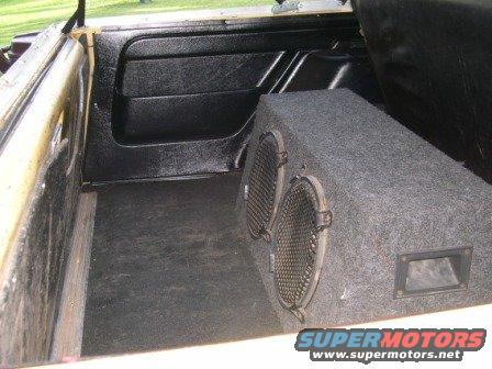 Interior cargo area of a vehicle with a gray carpeted subwoofer box and black door panel