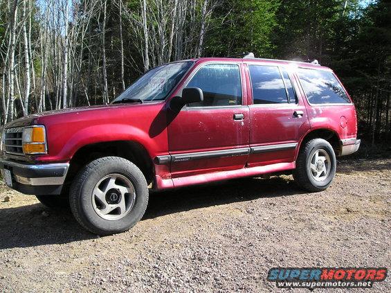 Red 1991 Ford Explorer parked on a gravel road with trees in the background