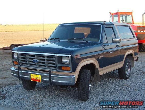 Dark blue and tan Ford Bronco parked on gravel, with a red tractor behind it
