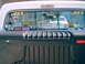 1969 Ford F-100 - Rear window of a white Ford F-100 pickup truck displays numerous aftermarket stickers and reflects another vehicle.