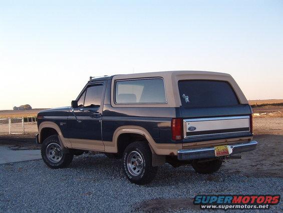 Rear view of a blue and tan Ford Bronco parked on gravel. License plate is visible