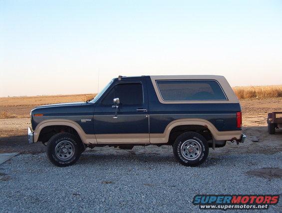 Blue and tan 1987 Ford Bronco SUV parked on gravel, side view
