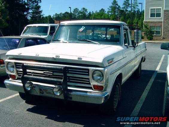 White 1969 Ford F-100 pickup truck with a black grille guard and two auxiliary lights parked in a lot