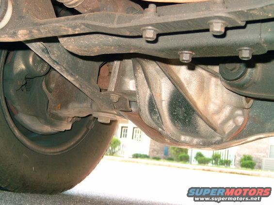 Underside view of a vehicle's rear axle and suspension components. Shows the differential housing, driveshaft, and part of the tire