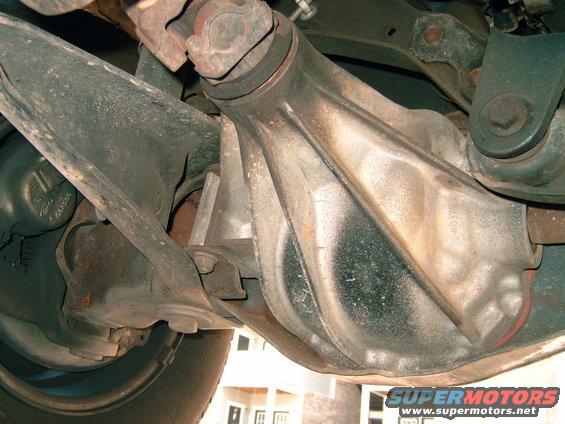 Underside view of a vehicle's rear axle housing, differential, and suspension parts. A 'SUPERMOTORS.NET' watermark is visible