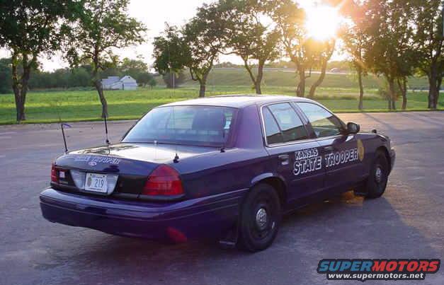 Purple 2001 Ford Crown Victoria police car, rear 3/4 view, parked outdoors with sun glare