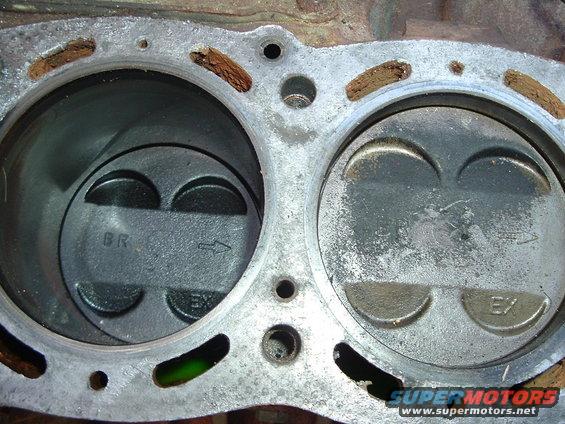 Engine block with two pistons, one marked BR, the other EX. Rusty gasket material visible