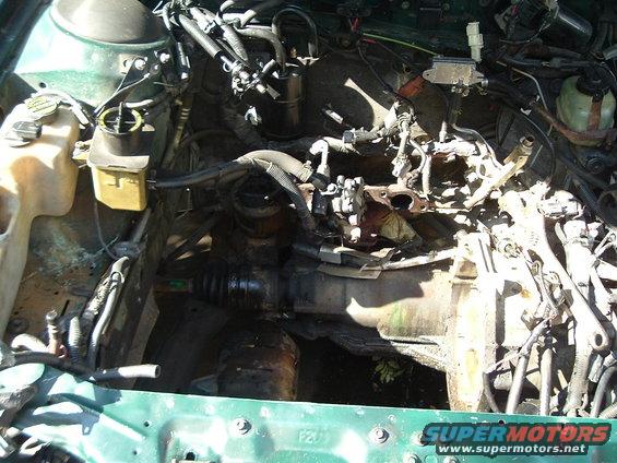 Engine bay with hoses, wires, and engine block visible. Some parts are removed