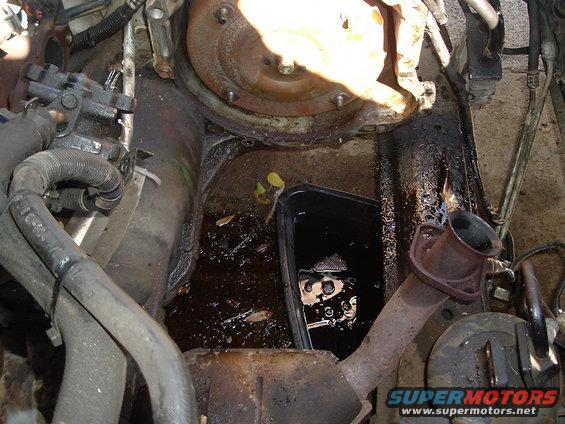 engine bay with oil pan and exhaust pipe, some oil spilled in a black pan