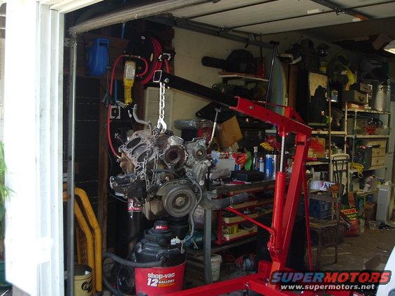 Engine suspended by a red engine hoist in a cluttered garage