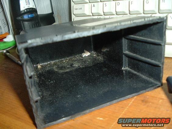 Close-up of a dirty, empty car interior storage compartment. A computer keyboard is visible in the background
