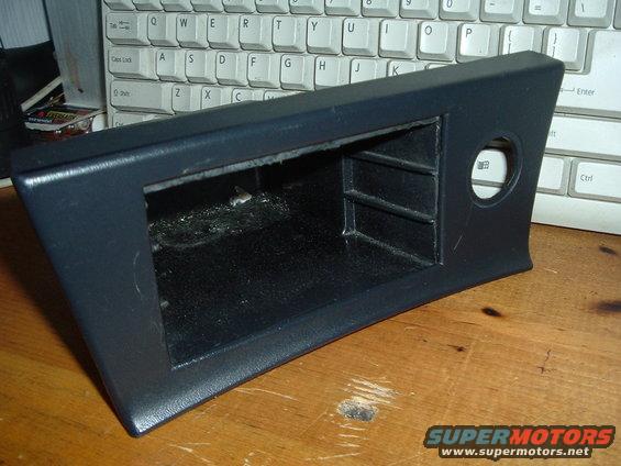 Dark gray center console trim piece with storage cubbies and a circular cutout