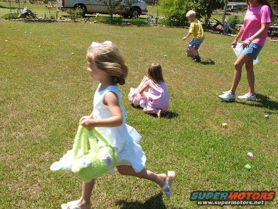 White pickup truck parked in a grassy yard with children hunting for Easter eggs