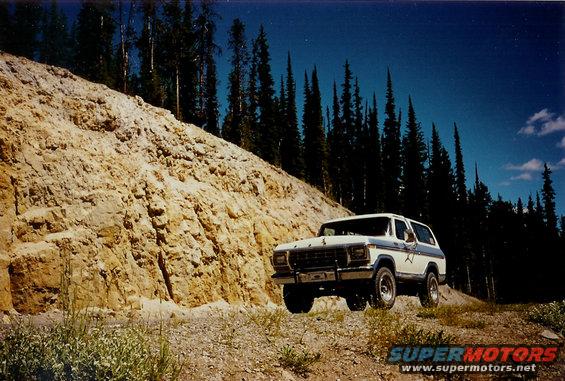 White 1978 Ford Bronco with blue stripe on a dirt road next to a rocky embankment