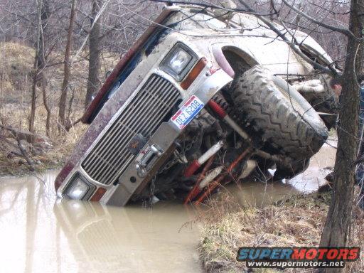 Vehicle stuck in muddy water, tilted on its side. License plate reads DEZ 6208
