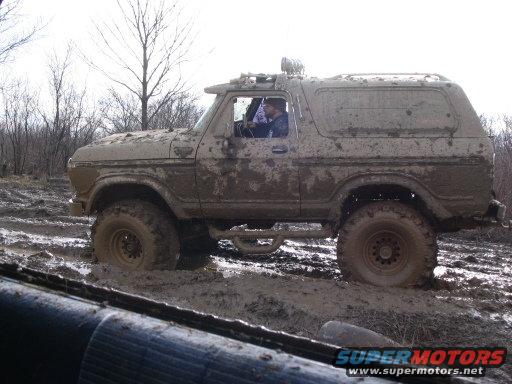 Muddy SUV stuck in a muddy trail, driver visible inside
