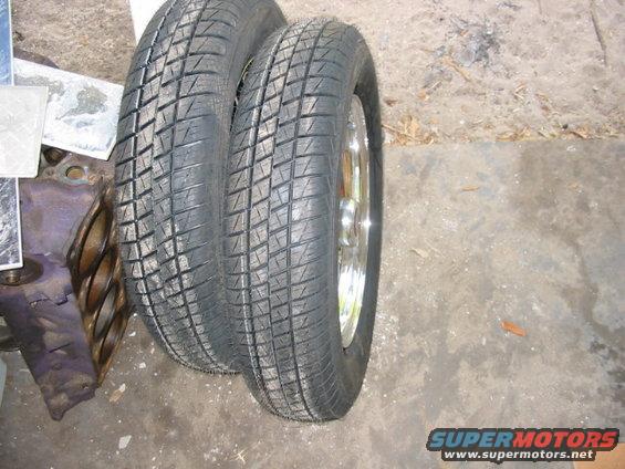 Two tires are leaning against a purple car engine block. One tire has a chrome rim