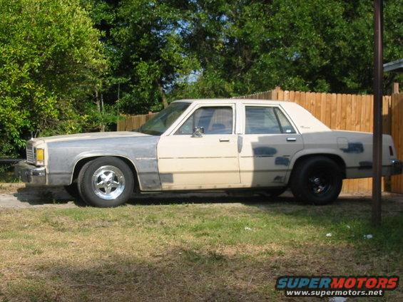 Side view of a beige sedan with primer-gray front fenders and mismatched rear wheels. 1985 Ford Crown Victoria LTD