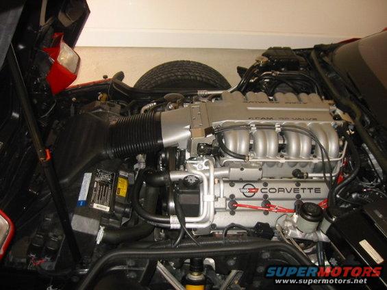 Corvette engine with silver intake manifold and "CORVETTE" text, red spark plug wires, tire visible behind