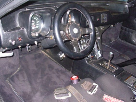 Black interior of a 1972 DeTomaso Pantera with racing harnesses and a custom steering wheel