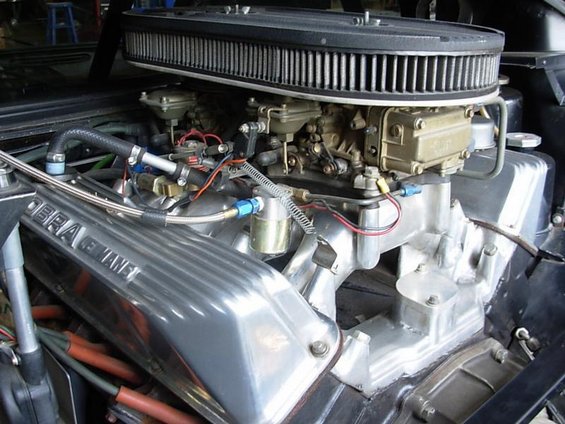 Close-up of a V8 engine with polished aluminum Cobra Manifold, dual carburetors, and air cleaner