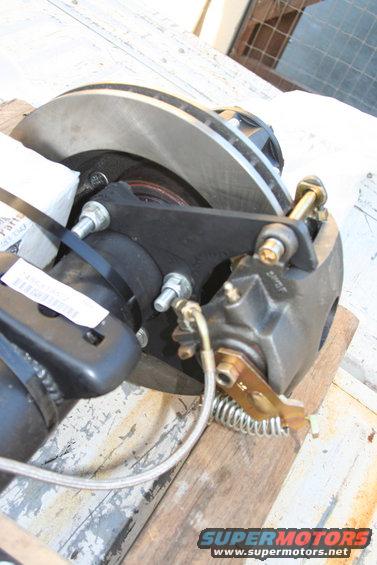 Rear disc brake assembly with caliper, rotor, and mounting bracket on wooden planks
