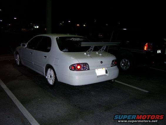White sedan with a large rear spoiler and aftermarket wheels parked at night