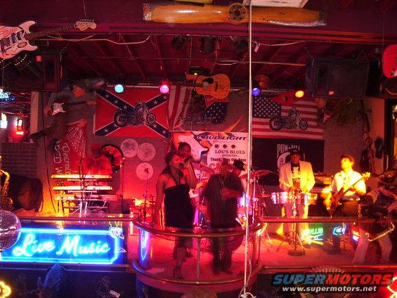 Live music stage with band, neon sign, and flags