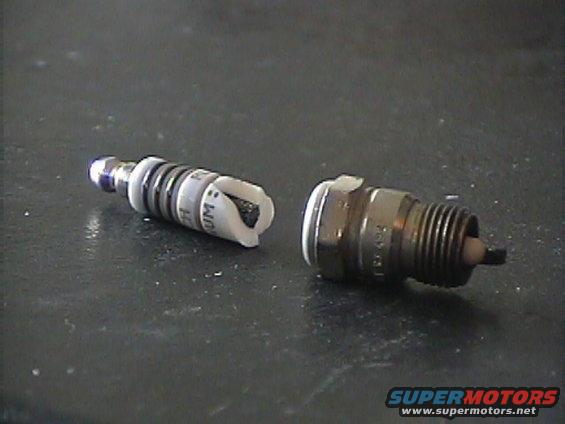 Two spark plugs, one with a broken ceramic insulator, on a dark surface