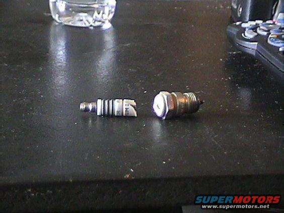 Two spark plugs on a dark surface, one broken