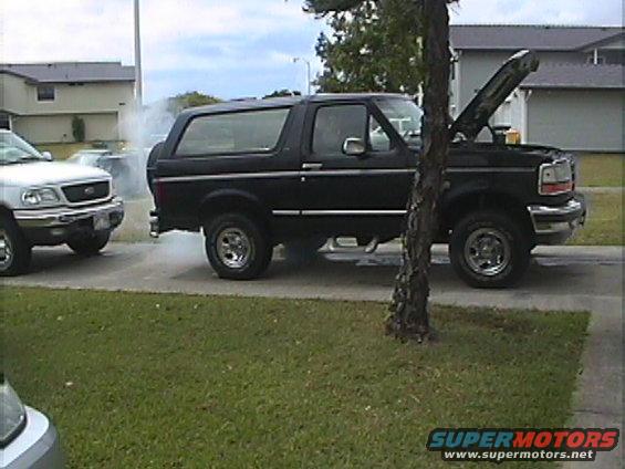 black 1994 Ford Bronco with hood up, smoke from engine, parked next to a silver Ford F-150