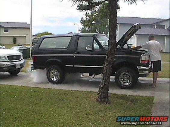 Black 1994 Ford Bronco with hood open, man looking at engine. Another white truck is parked nearby