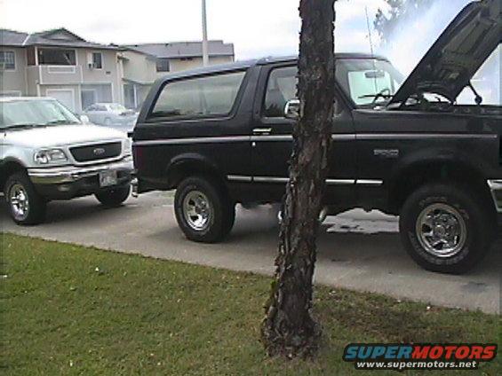Black SUV with hood up, parked next to a silver pickup truck