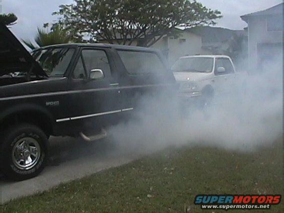 Black 1994 Ford Bronco with hood open, emitting smoke, parked next to a white SUV