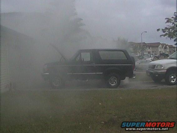 Black Ford Bronco with hood open, side view, surrounded by smoke