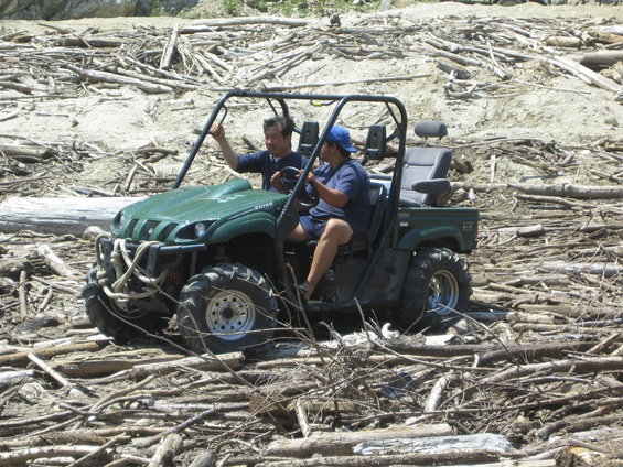 Two guys in a green UTV driving through a debris field