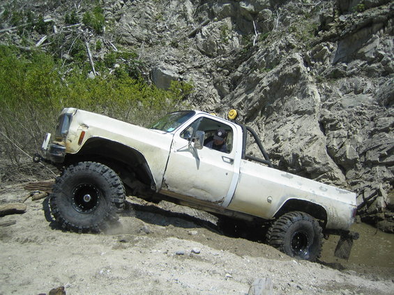 White pickup truck with big tires going through mud on a rocky hill
