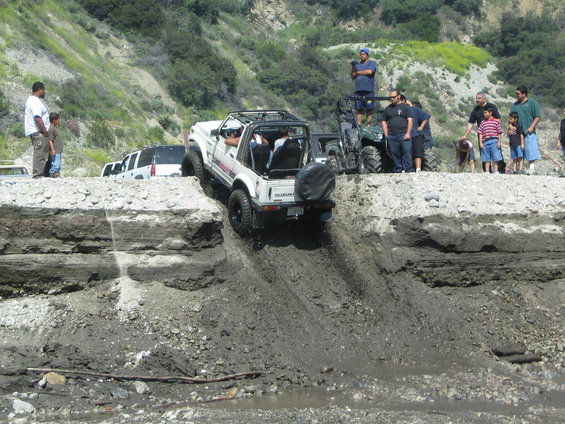 Suzuki Samurai going down a muddy hill, people watching