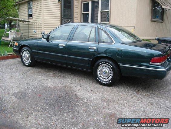 1996 Ford Crown Victoria sedan, dark green, parked on asphalt in front of a house