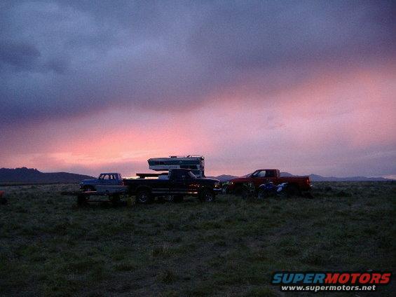 Multiple trucks and an RV parked in a field at sunset
