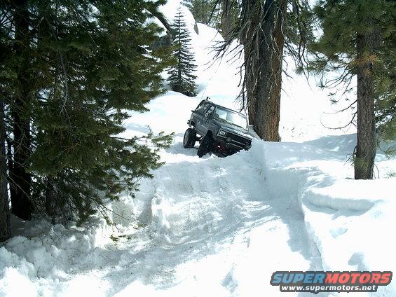 Dark colored off-road SUV driving through deep snow on a mountain trail