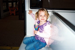 Little girl with pigtails holding a drink while sitting on a bench inside