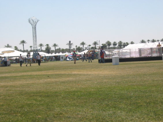 Outdoor festival with tents, people walking, and a tall metal sculpture