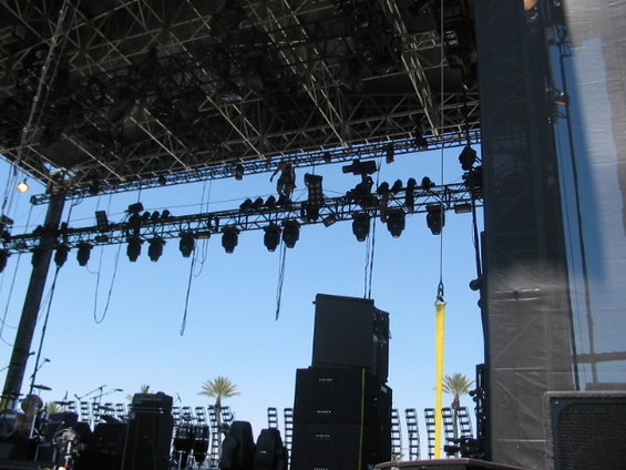 Stage lighting rig with speakers and palm trees under a clear blue sky