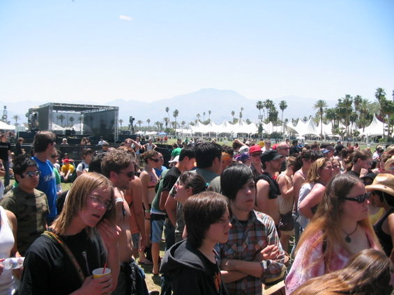 Crowd of people gathered outdoors with tents and a stage in the background