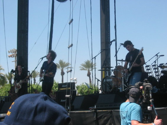Band performing on an outdoor stage with palm trees in the background