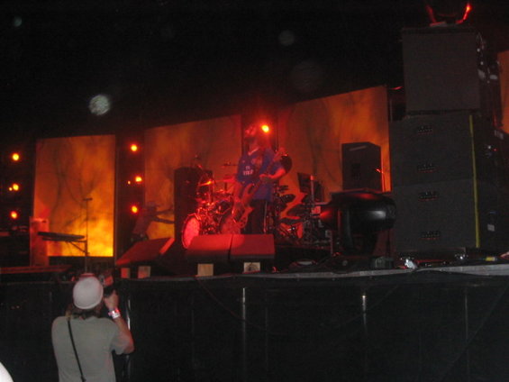 Photographer in foreground taking picture of band performing on stage with orange lighting
