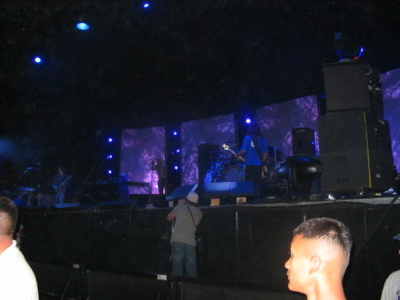 Band performing live on a stage with large screens displaying abstract purple graphics