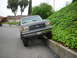 1988 Ford Bronco - This Ford Bronco is parked with its front wheels on a concrete curb next to a grassy hill.
