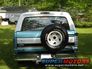 Rear of a teal and white Ford Bronco with a spare tire mounted on the back. Some text is visible on the rear window